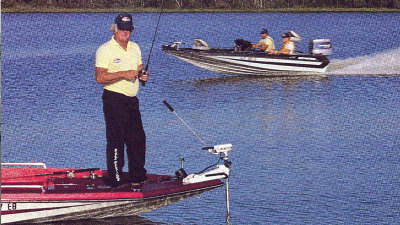 Man fishing with boat cruising through water behind him